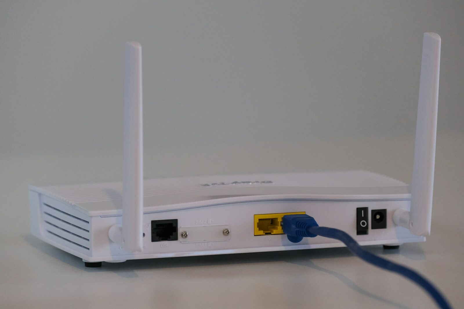 Rückseite eines weißen Routers, in dessen LAN-Buchse ein blaues Netzwerkkabel steckt