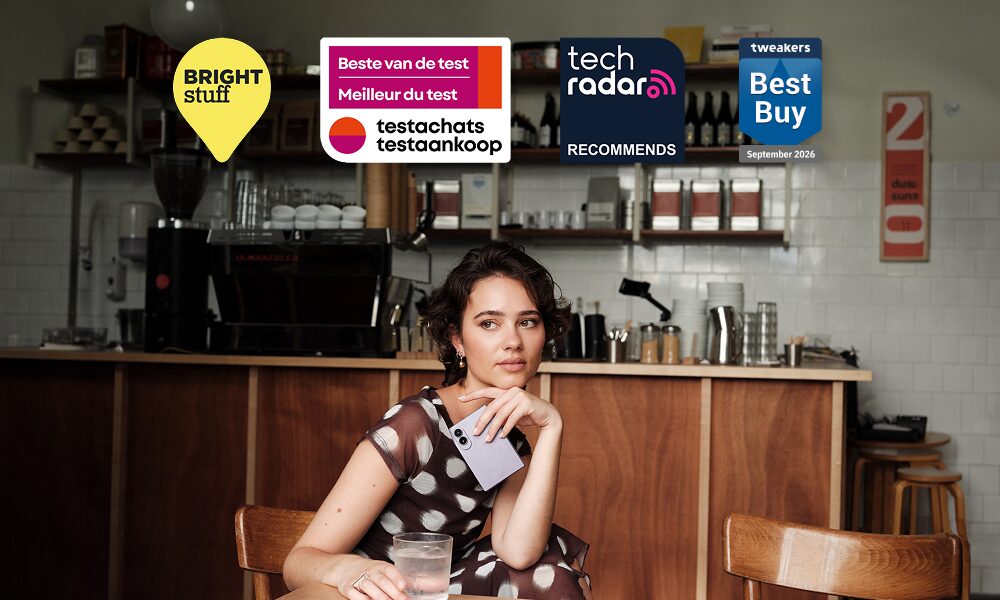 Vrouw in een café met een dichtgevouwen Galaxy Z Fold8, daarboven de logo's van Bright, Testaankoop, TechRadar en Tweakers