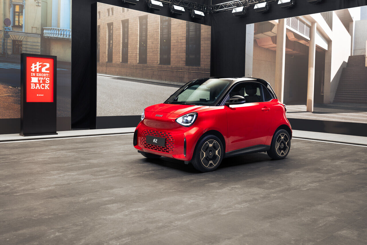 Roter smart #2 Premium mit schwarzem Dach in einer Ausstellungshalle, daneben eine Stele mit der Aufschrift „#2 in short: it's back“
