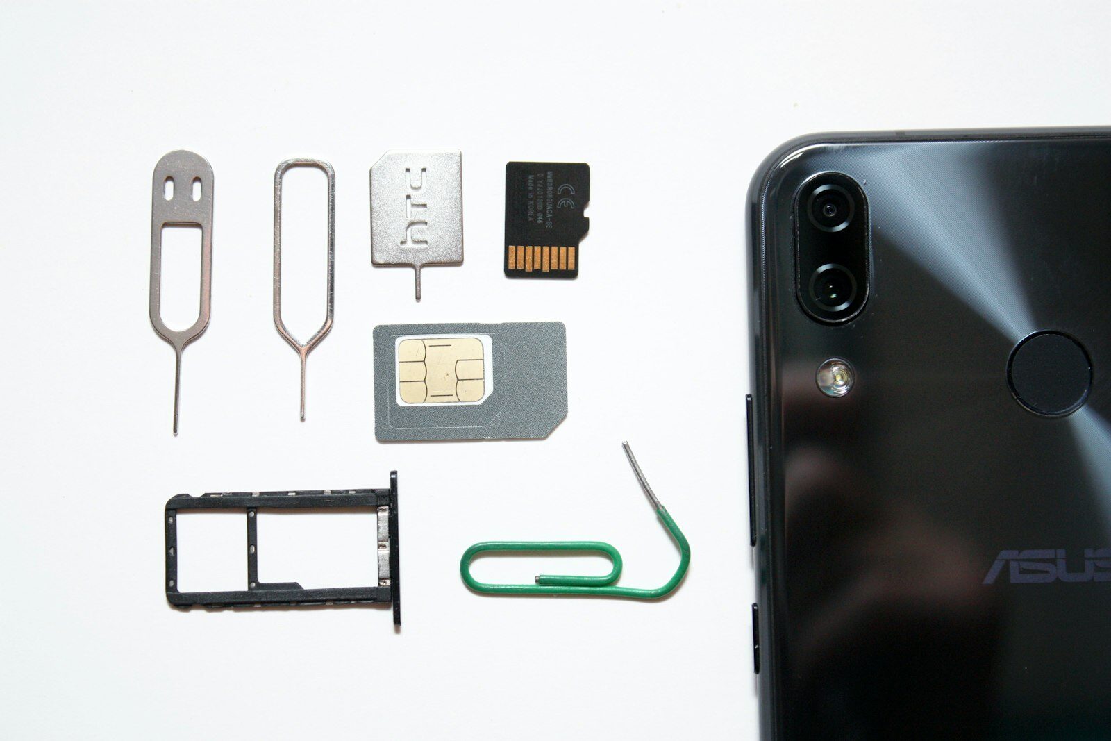 Smartphone-Rückseite neben SIM-Karte, Speicherkarte, SIM-Schacht und SIM-Nadeln auf weißem Untergrund