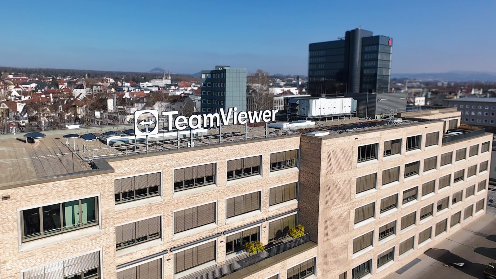 Bürogebäude von TeamViewer mit großem Firmenlogo auf dem Dach, im Hintergrund Stadt und Hügel unter blauem Himmel