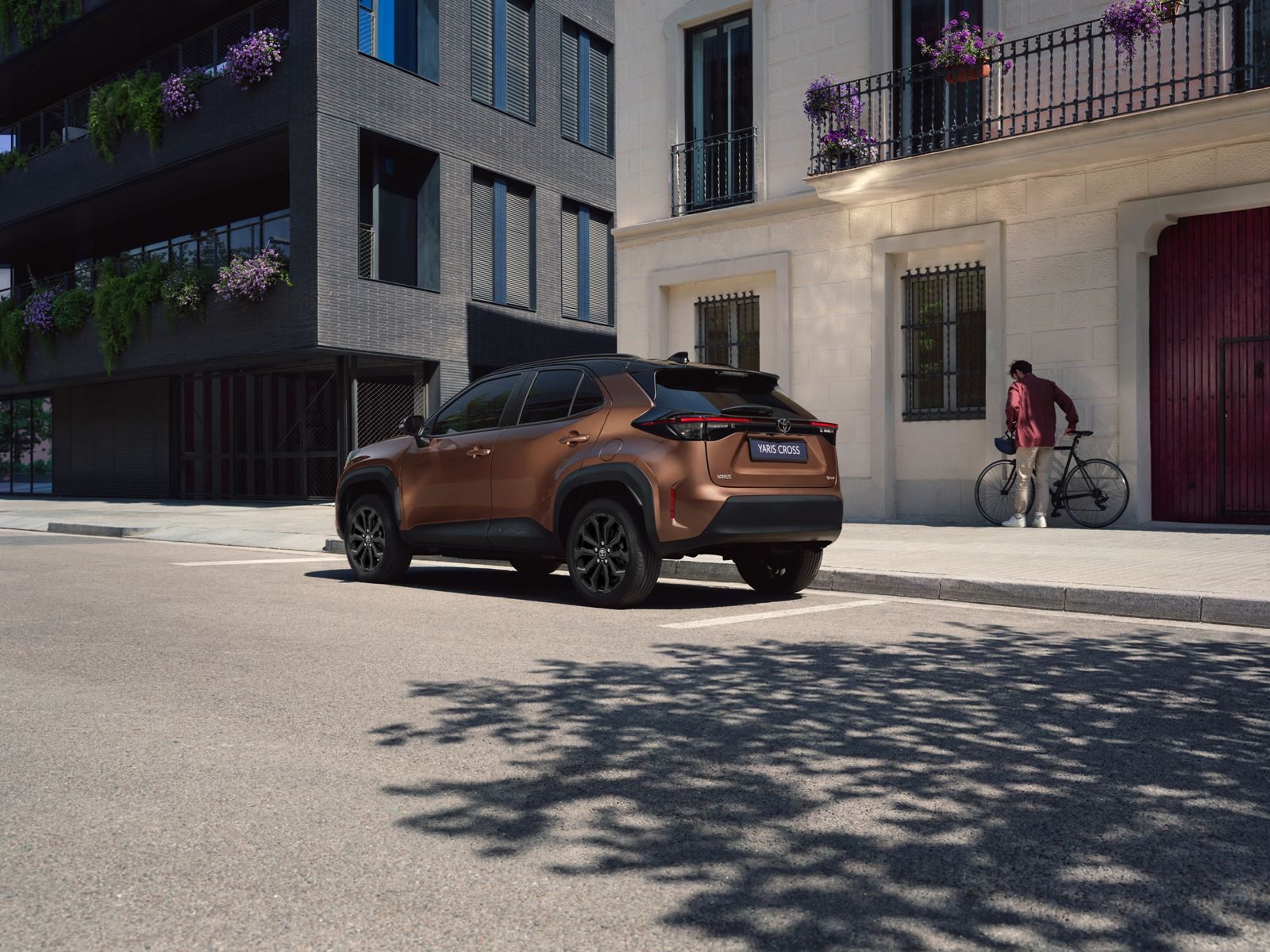 Bronz renkli Yaris Cross Hybrid'in arkadan çapraz görünümü, siyah jantlar ve siyah tavanla