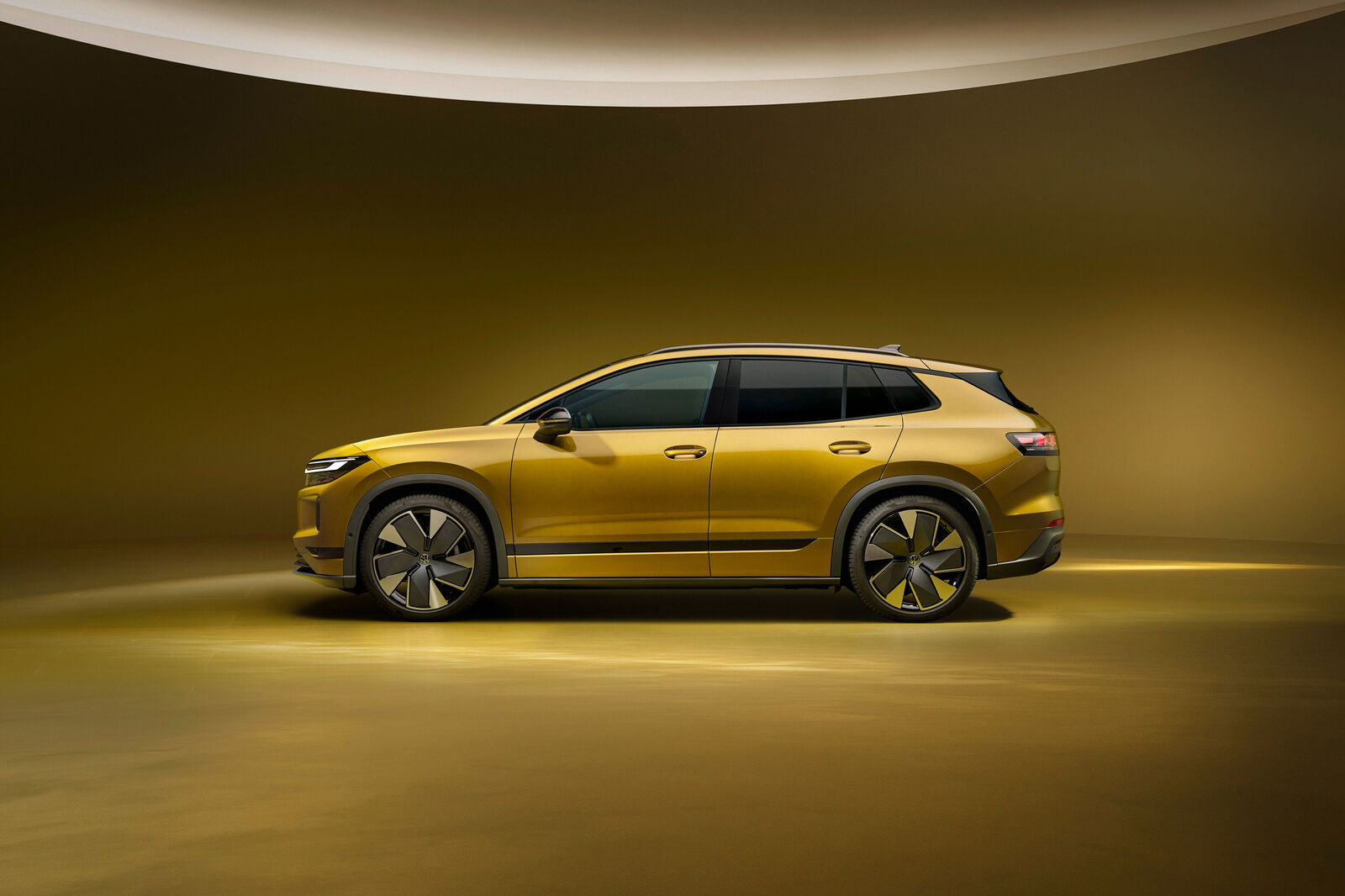 Goldfarbenes Elektro-SUV von Volkswagen in der Seitenansicht vor einem warm ausgeleuchteten Studiohintergrund