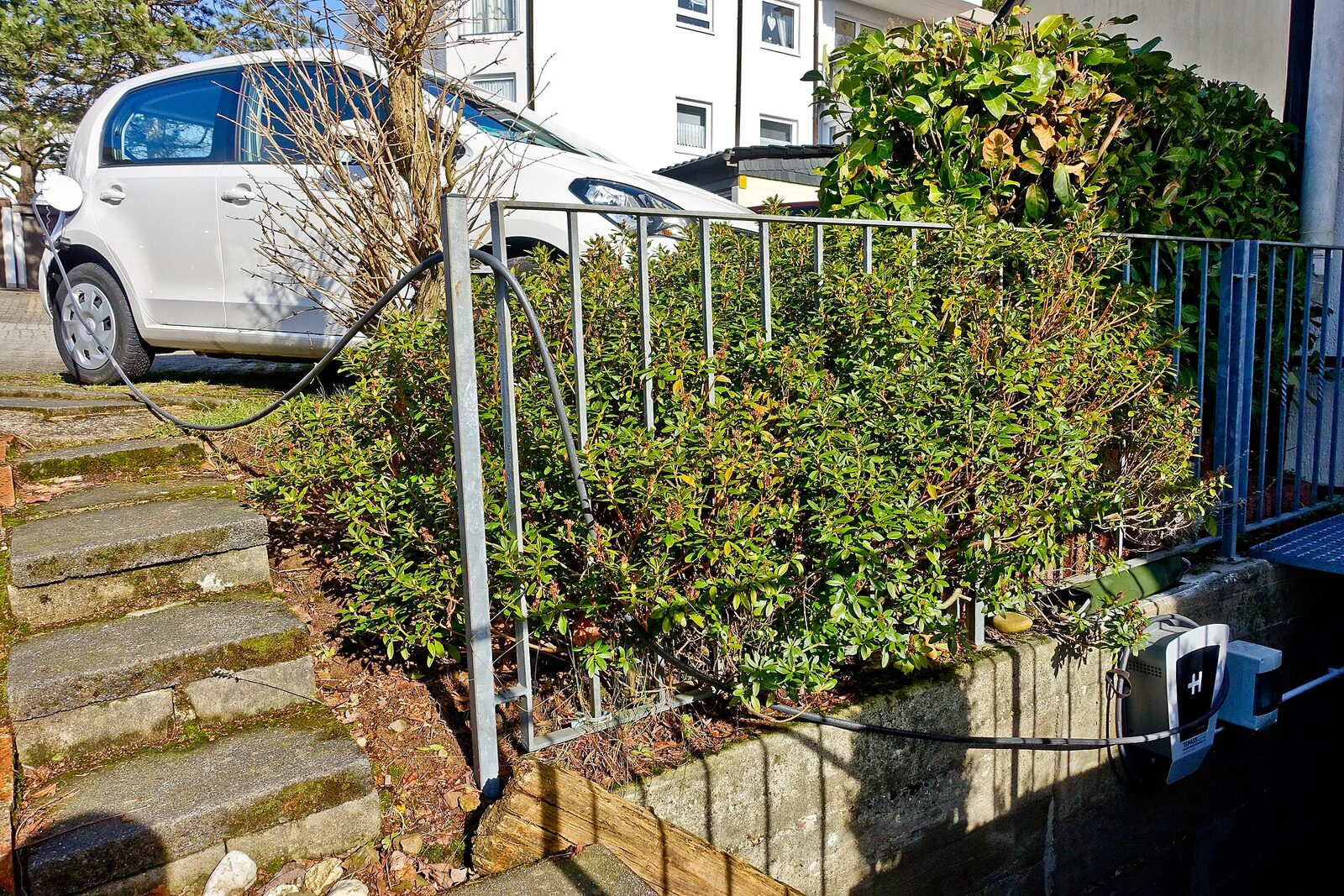 Private Wallbox an einer Gartenmauer lädt einen weißen Kleinwagen